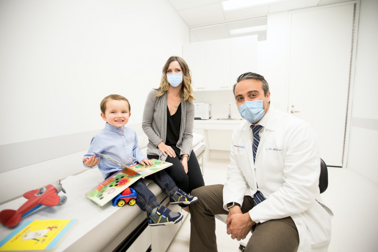 医生和女人，戴着口罩，带着年幼的儿子在医生的办公室就诊